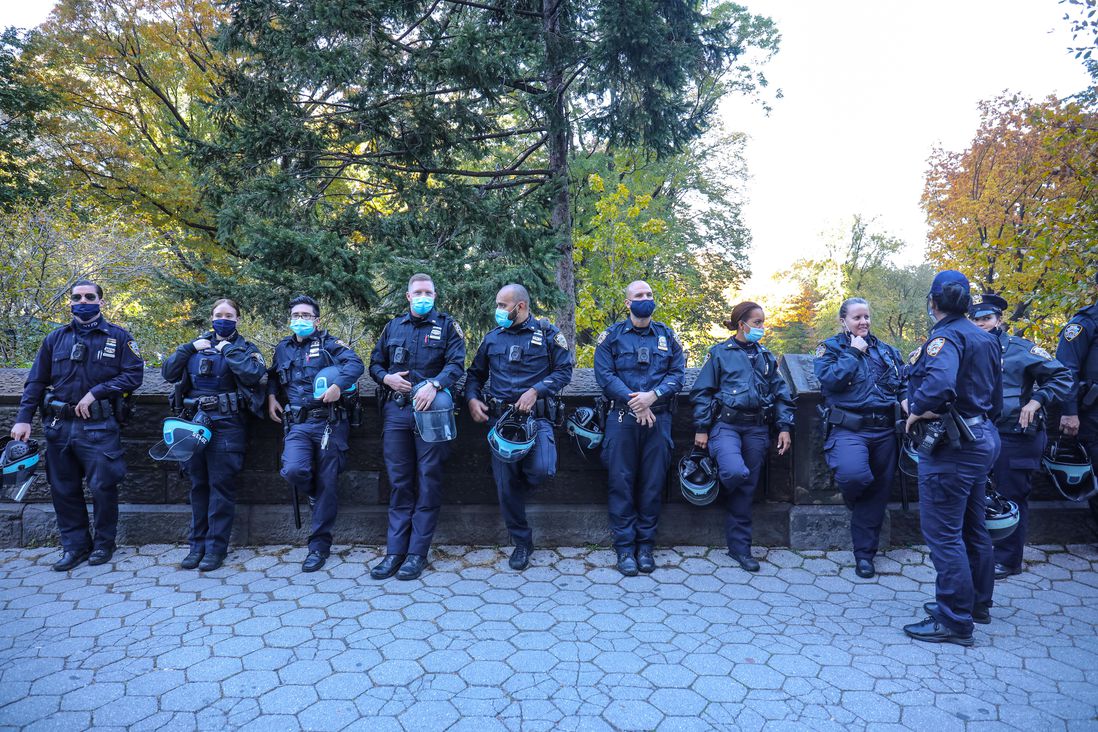 A dozen police officers lean against a fence at Central Park